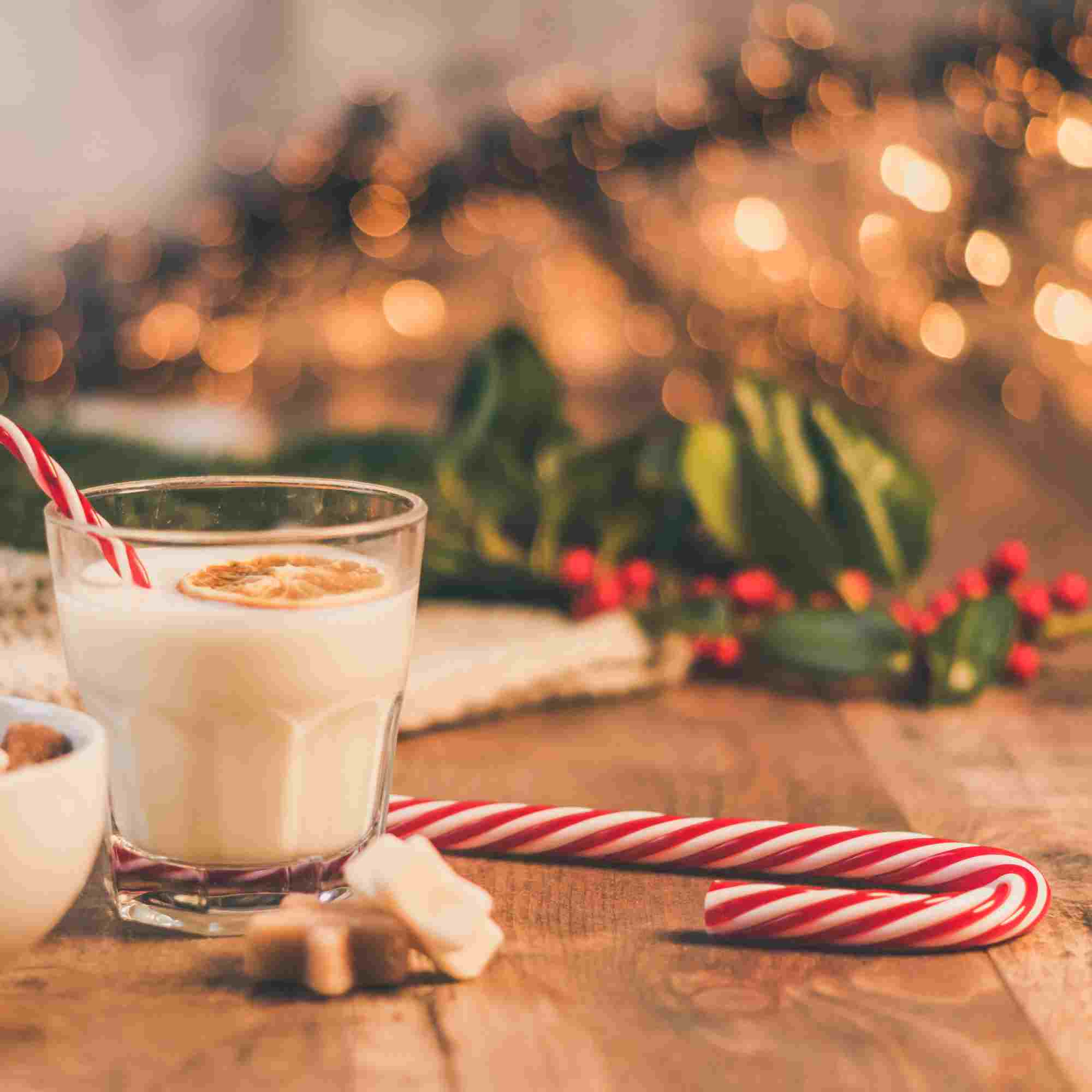 A glass of milk with candy canes on a wooden table.