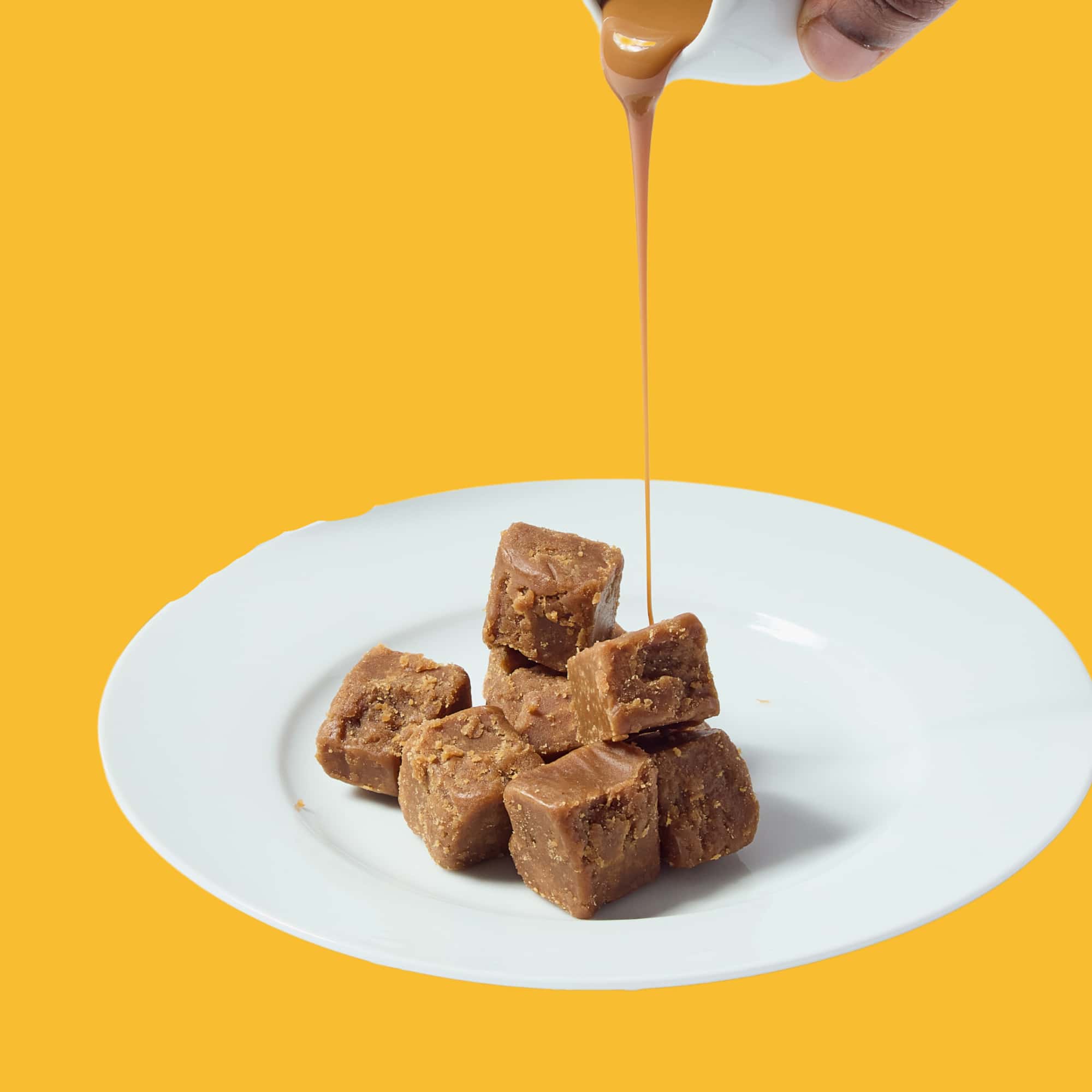 A person is pouring caramel over a plate of fudge.