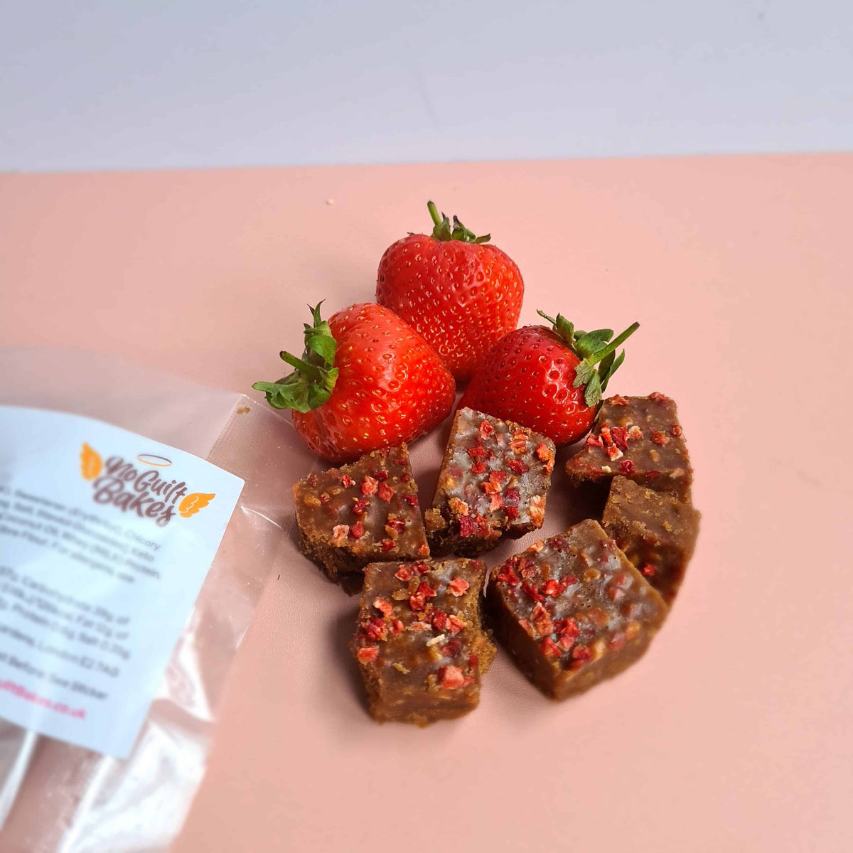 An ultimate sweet treat trio featuring a bag of No Guilt Bakes Keto Fudge Bundle and a bag of Belgian Caramel Keto Fudge, topped with fresh strawberries.